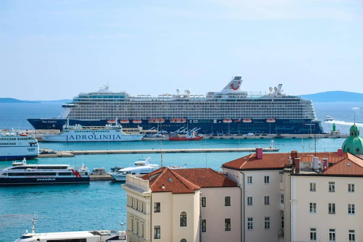 Panoramic view of Split’s harbor with multiple ferries, including a Jadrolinija vessel, docked near the historic old town and cruise ships in the background.