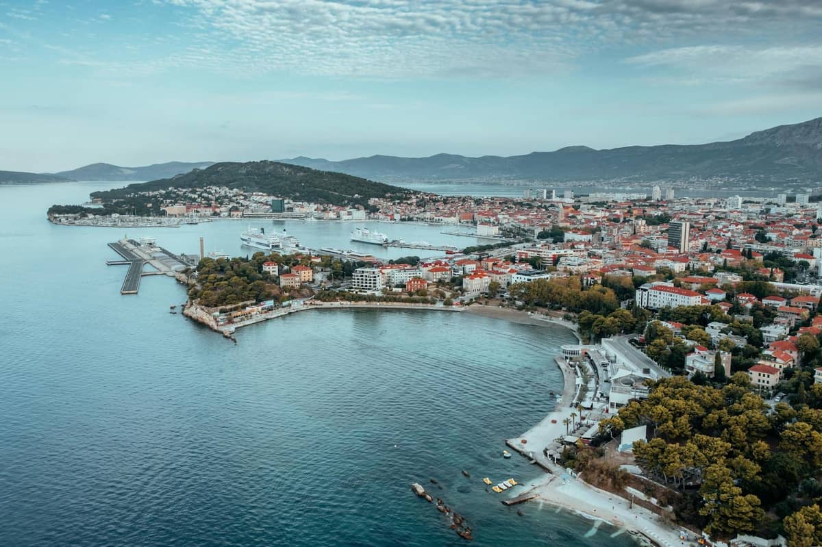 Luftaufnahme von Split mit dem bewaldeten Hügel Marjan, der Altstadt, dem Hafen und der Küstenlinie, die das Gebiet jenseits der Palastmauern hervorhebt.