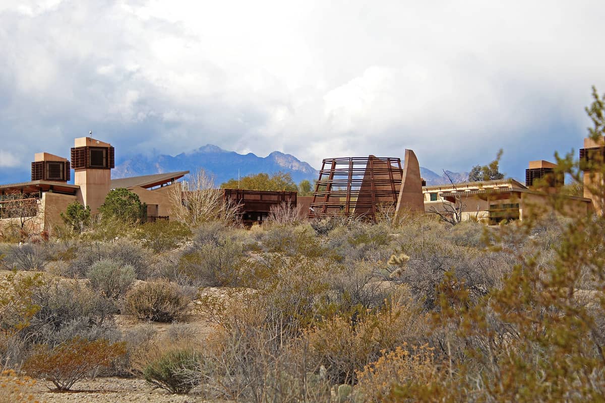 Bangunan khas Springs Preserve di Las Vegas berdiri di antara vegetasi gurun dan pegunungan di bawah langit berawan sebagian.