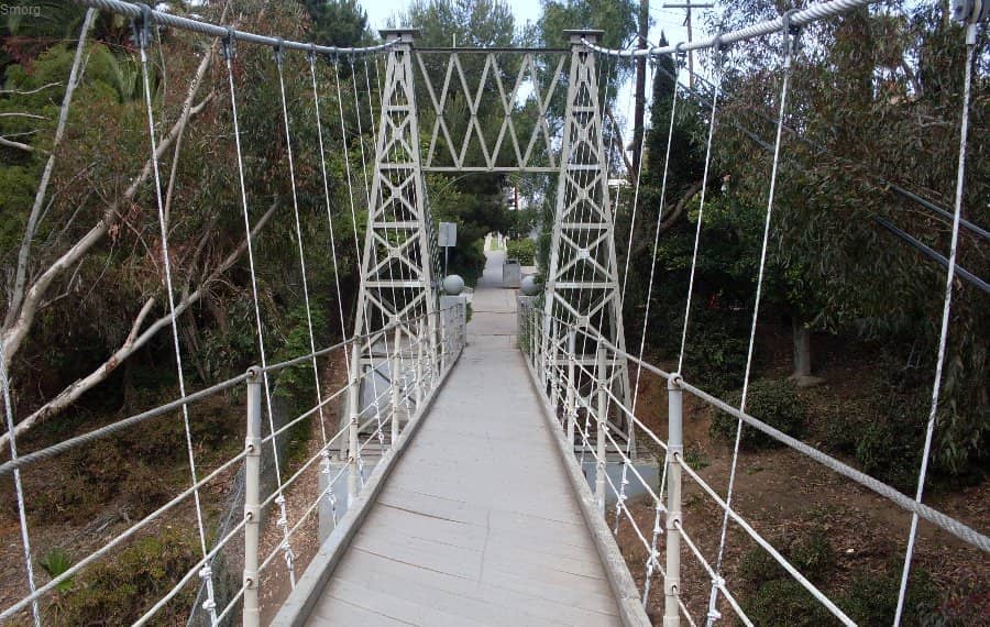 Die Spruce Street Suspension Bridge in San Diego erstreckt sich über eine bewaldete Schlucht, gerahmt von weißen Geländern und umgeben von Eukalyptus und Grünpflanzen.
