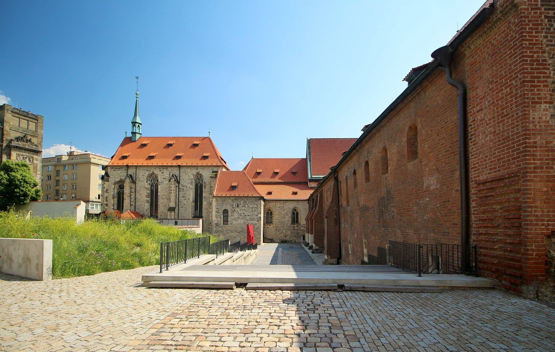 Das St.-Agnes-Kloster in Prag zeigt gotische Steinarchitektur, rote Dächer und Kopfsteinpflasterwege unter einem strahlend blauen Sommerhimmel.
