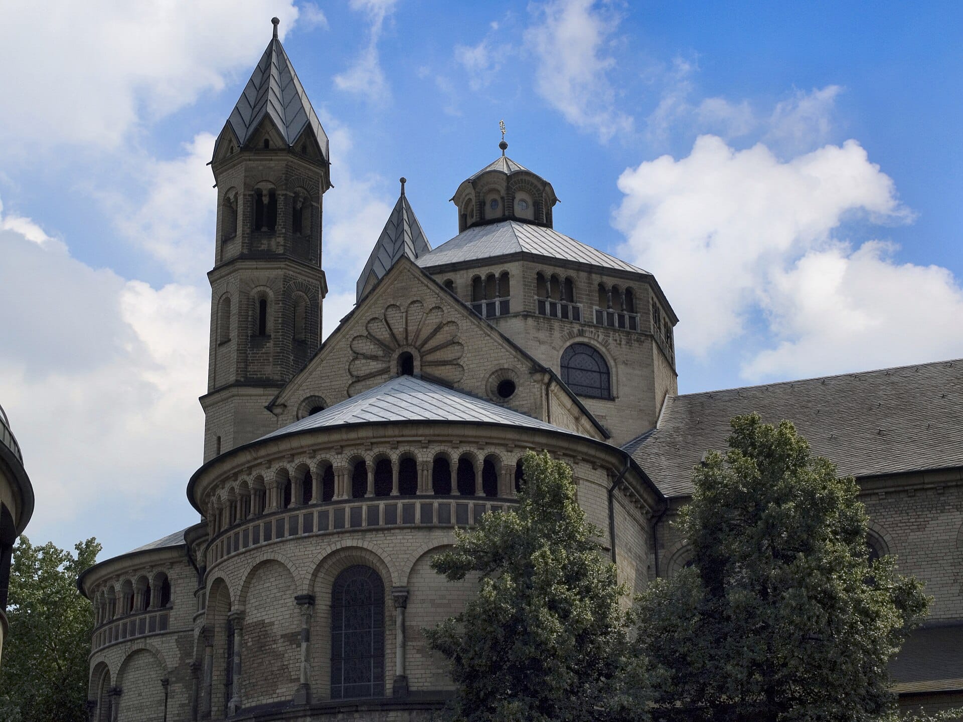 มุมมองภายนอกของโบสถ์ St. Aposteln เมืองโคโลญ เผยให้เห็นตัวโบสถ์แบบโรมาเนสก์ ส่วนอะพส์โค้ง และหอคอยใต้ท้องฟ้าสีฟ้าปนเมฆขาวบาง