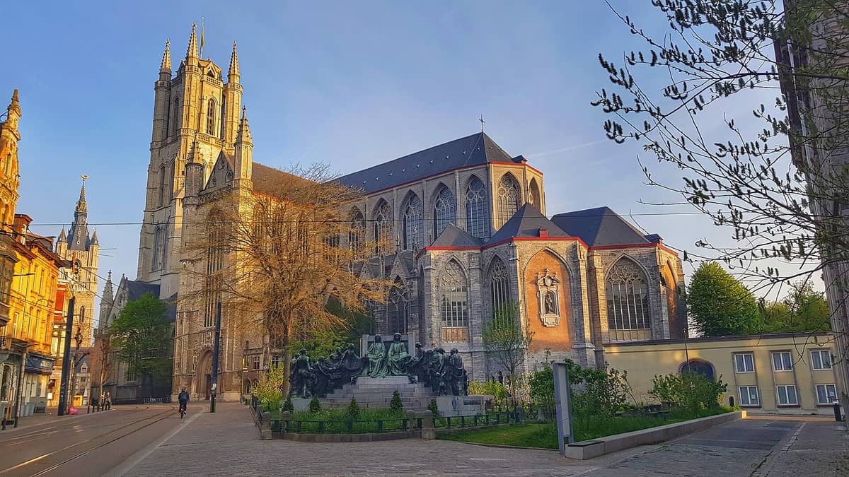 St Bavo's Cathedral in Ghent, Belgium, photographed from the side with its Gothic architecture illuminated in golden light, featuring intricate windows and statues.
