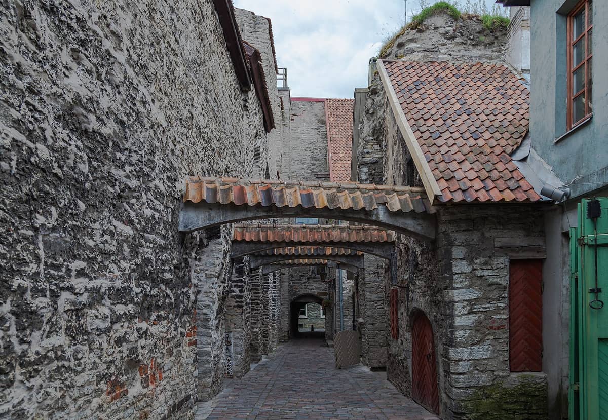 Der Katharinengang in Tallinns Altstadt – eine schmale mittelalterliche Kopfsteinpflastergasse mit rauen Steinmauern, roten Ziegelbögen und historischen Holztüren.