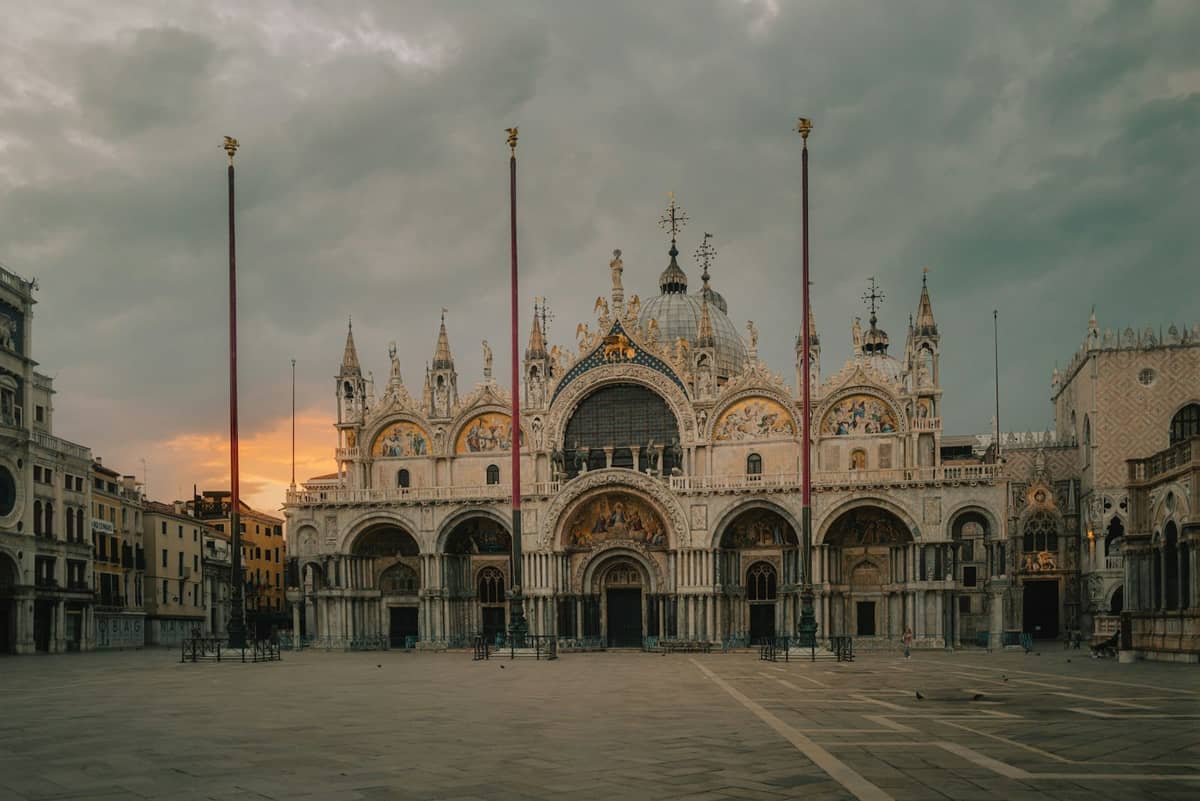 Weitwinkelpanorama der prunkvollen Westfassade des Markusdoms in Venedig bei Sonnenaufgang – mit Kuppeln, Bögen und goldenen Mosaiken über dem menschenleeren Platz.