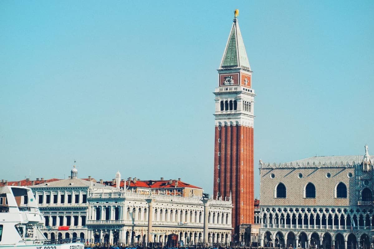 Der Campanile di San Marco erhebt sich über die historischen venezianischen Gebäude und die Uferpromenade, vor einem klaren blauen Himmel.