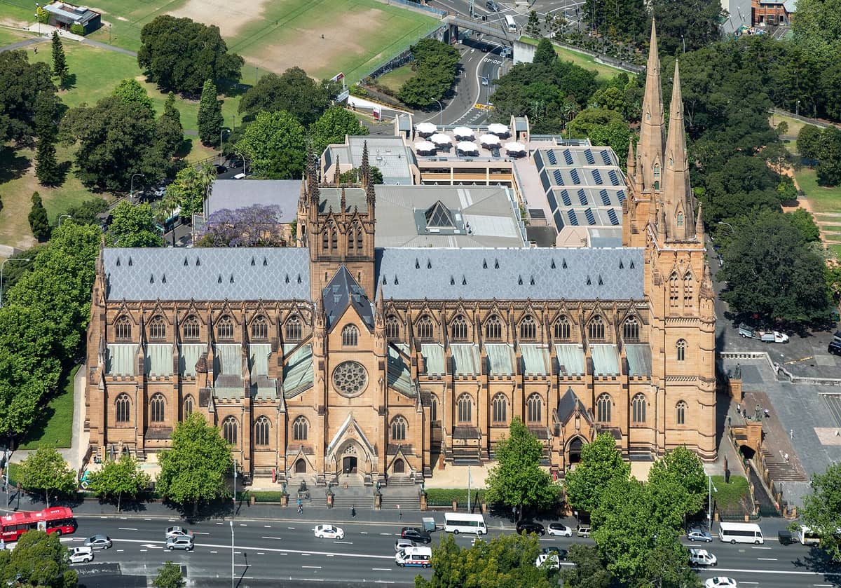 Vista aerea della Cattedrale di St Mary a Sydney che mostra l'intera lunghezza dell'edificio neogotico, le sue torri campanarie gemelle e il verde circostante in una giornata di sole.