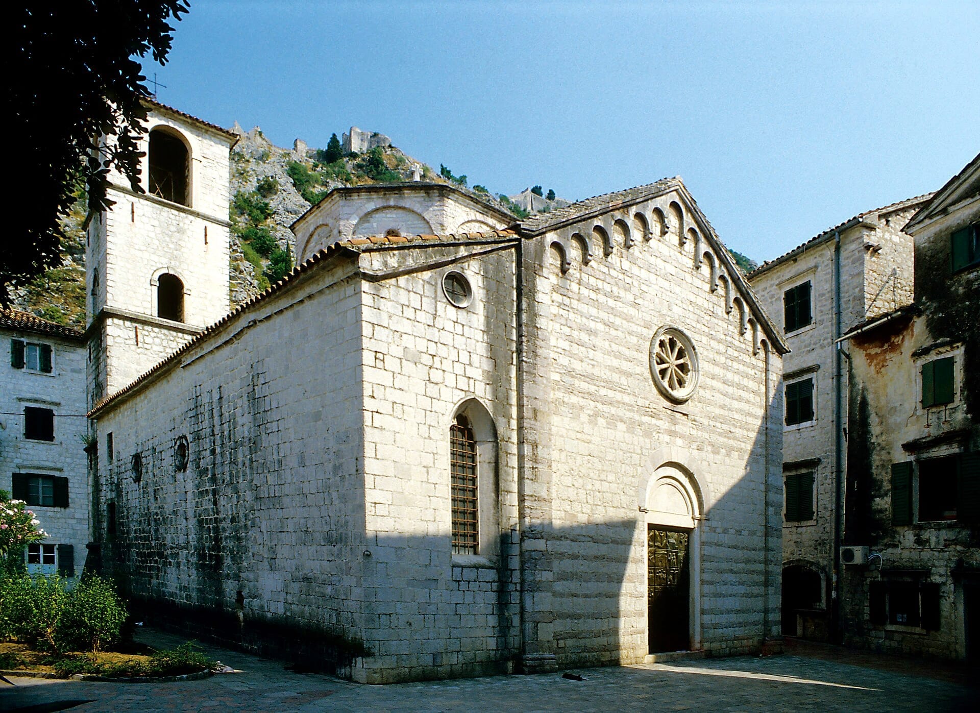 Vista esterna della Chiesa Collegiata di Santa Maria a Kotor, con architettura romanica in pietra, rosone e campanile sotto un cielo azzurro limpido.