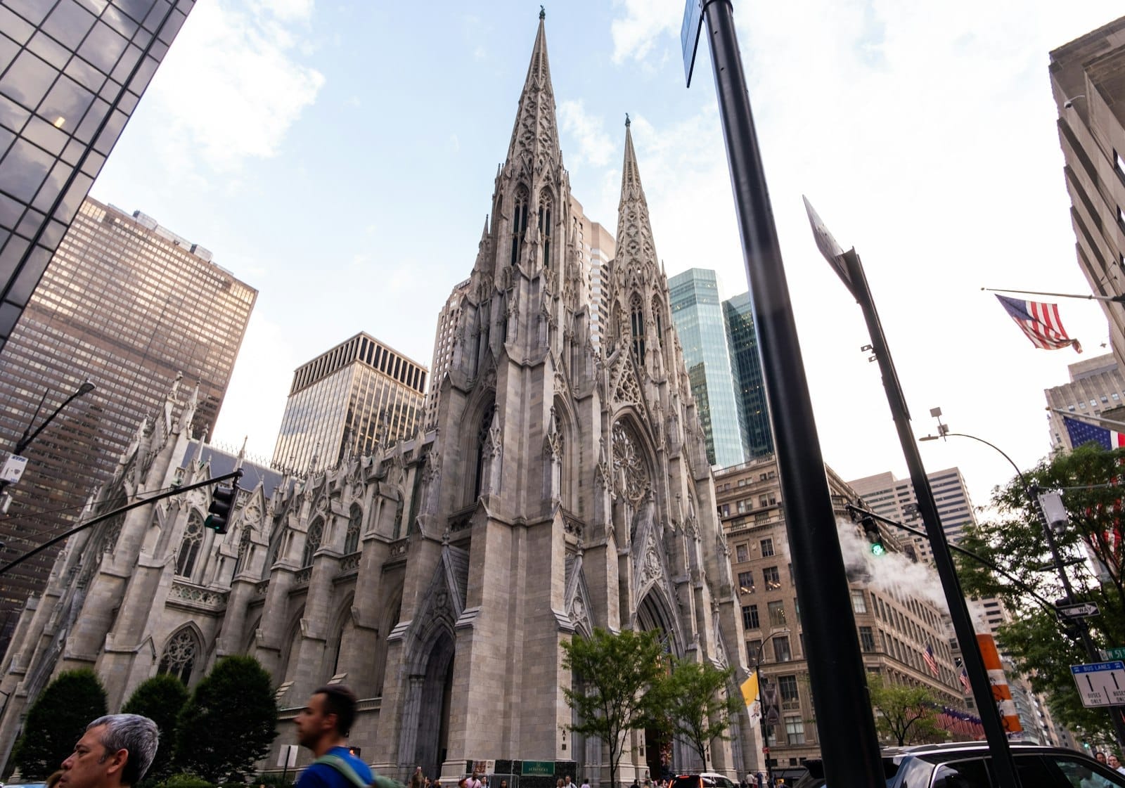 Vista ampia della Cattedrale di San Patrizio incorniciata dai grattacieli di vetro della Fifth Avenue a Midtown Manhattan, con persone e vita cittadina in primo piano.