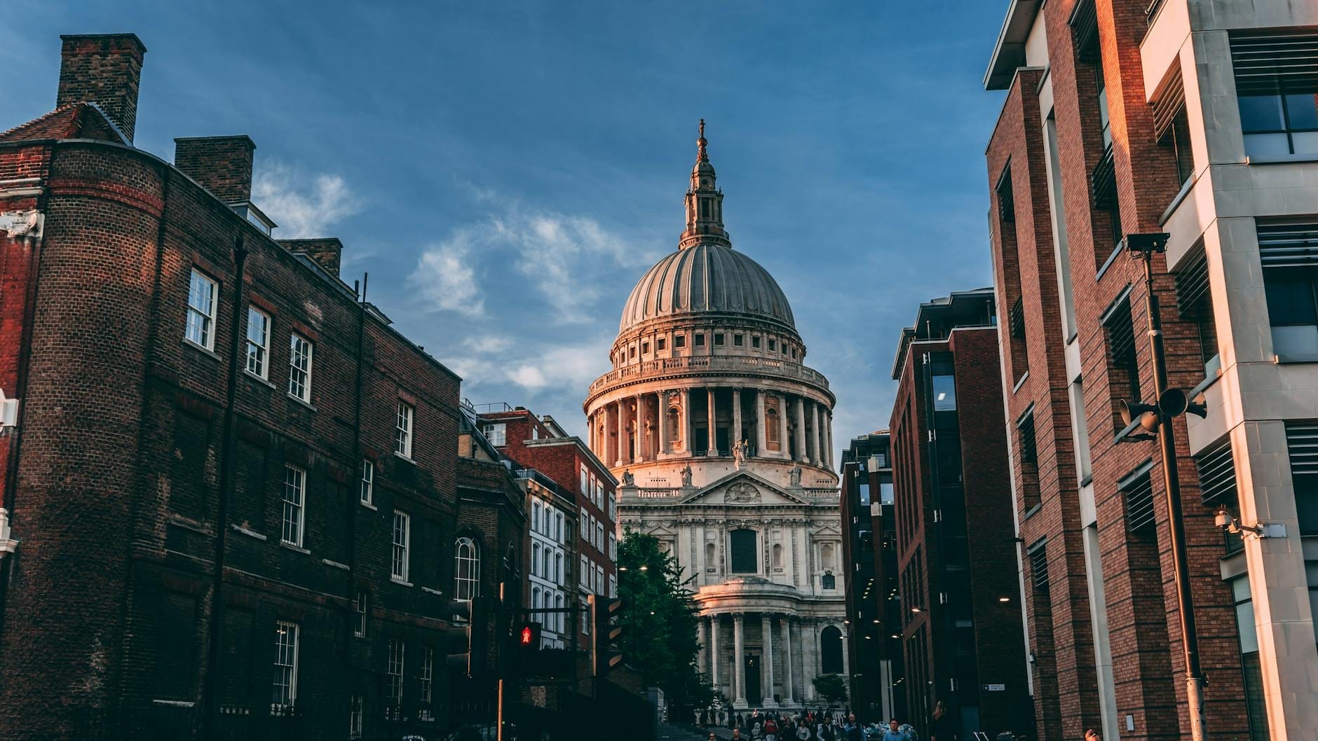 La Cattedrale di St Paul incorniciata da edifici storici e moderni in una via di Londra al tramonto, con l'iconica cupola che si staglia su un cielo blu intenso.
