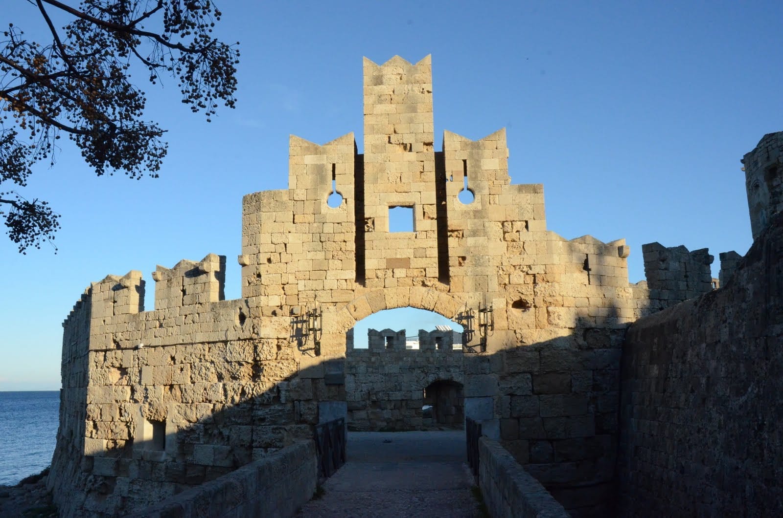 ประตู St Paul's Gate ในเมือง Rhodes ประตูหินยุคกลางที่มีใบเสมาและลวดลายแกะสลัก ตั้งตระหง่านอยู่ใต้ท้องฟ้าสีฟ้าแจ่มใสริมทะเล