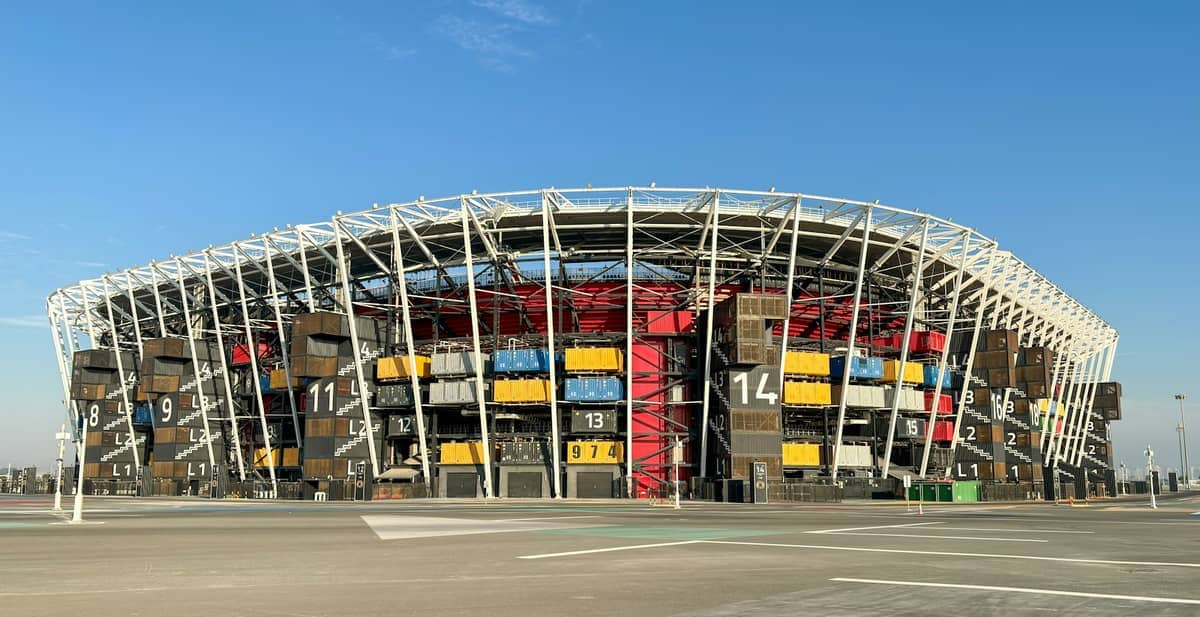 Das Stadium 974 in Doha, aus bunten Schiffscontainern erbaut, steht unter einem klaren blauen Himmel mit seiner markanten geometrischen Struktur.