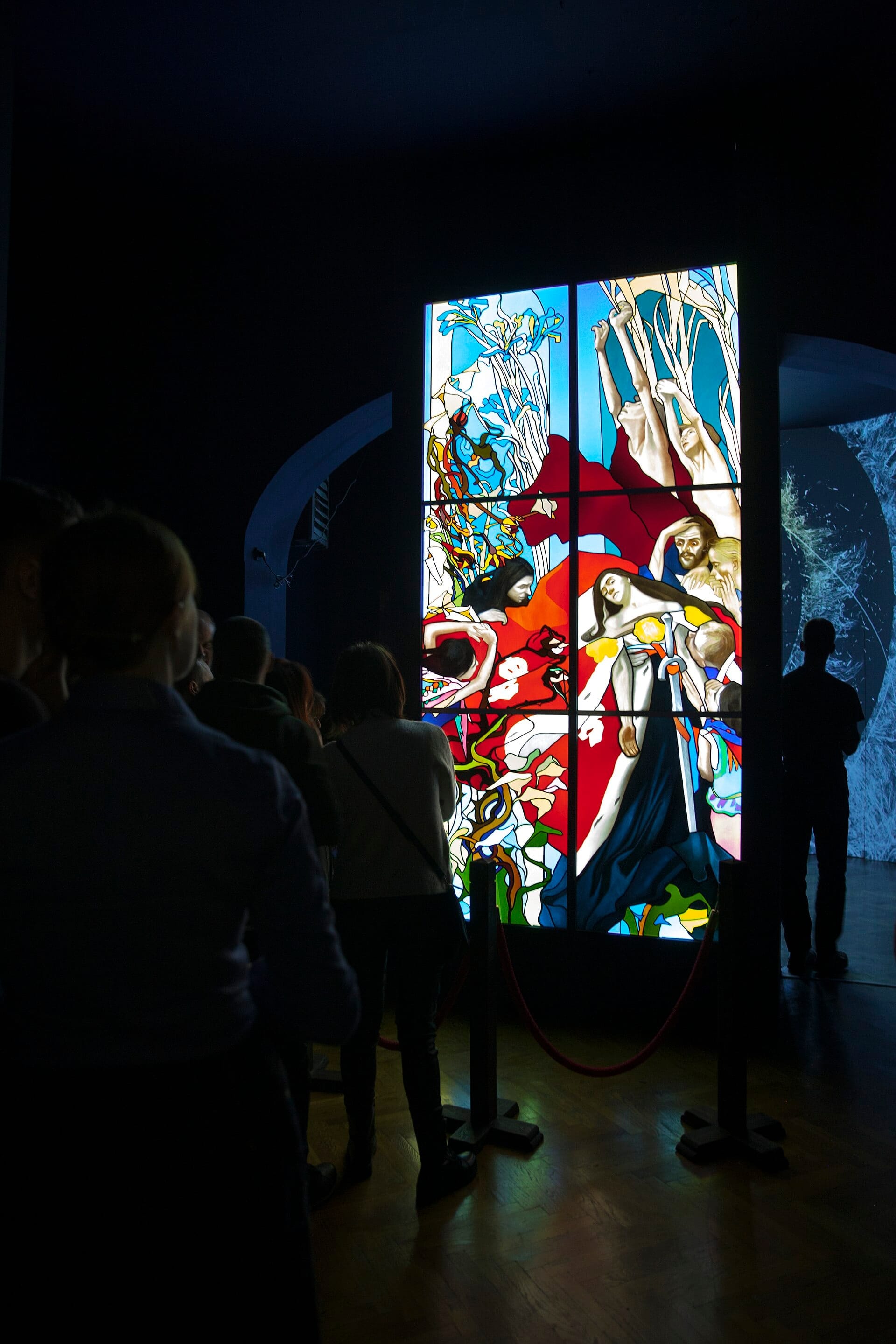 ผู้เยี่ยมชมชมผลงานศิลปะกระจกสีขนาดใหญ่ที่ส่องสว่างใน Stained Glass Museum Kraków พร้อมสีสันสดใสและรูปร่างมนุษย์ที่ซับซ้อน