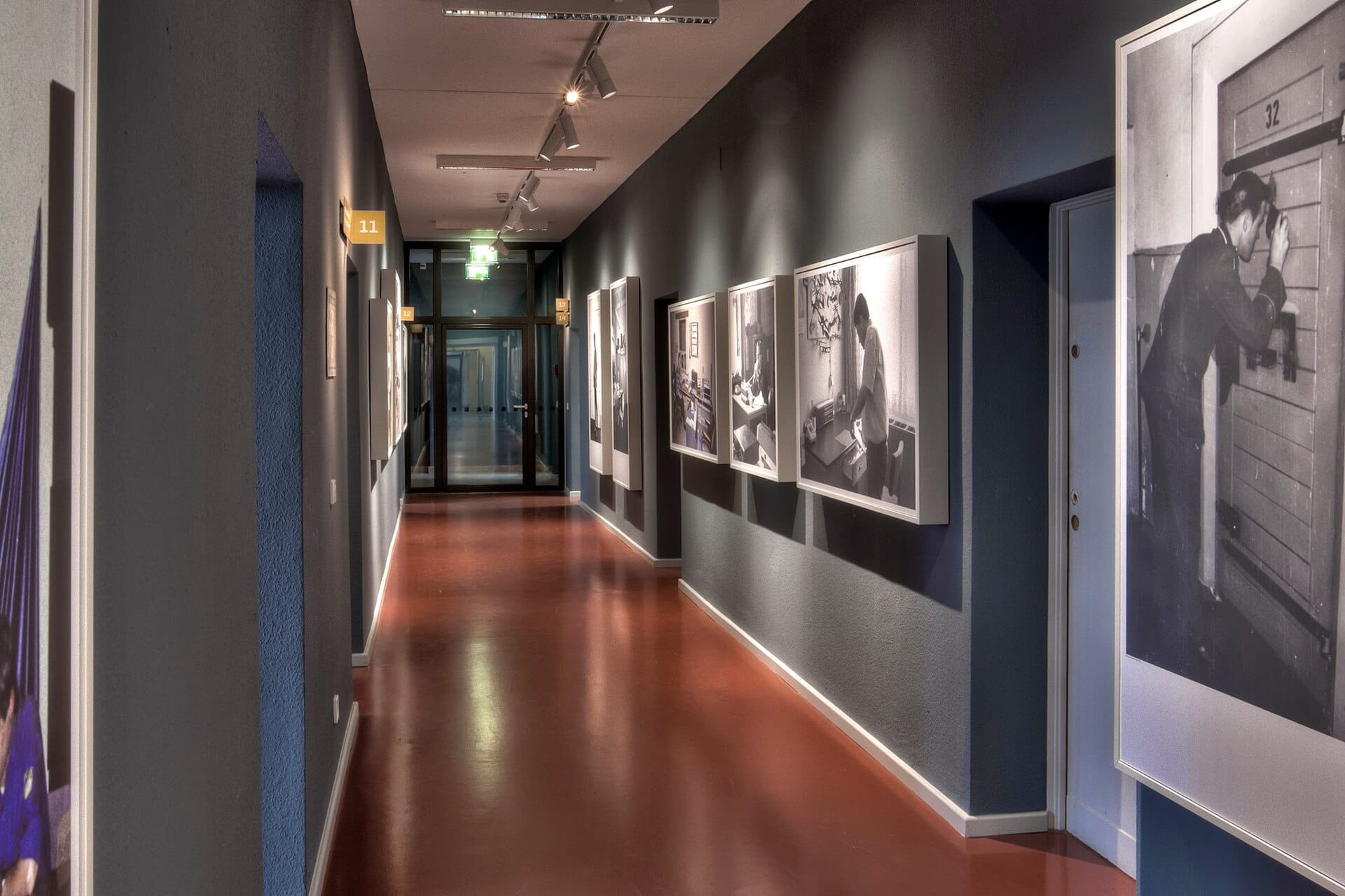 Un corridoio ben illuminato nello Stasi Museum Berlin, con fotografie vintage in bianco e nero esposte su pareti blu tenue.