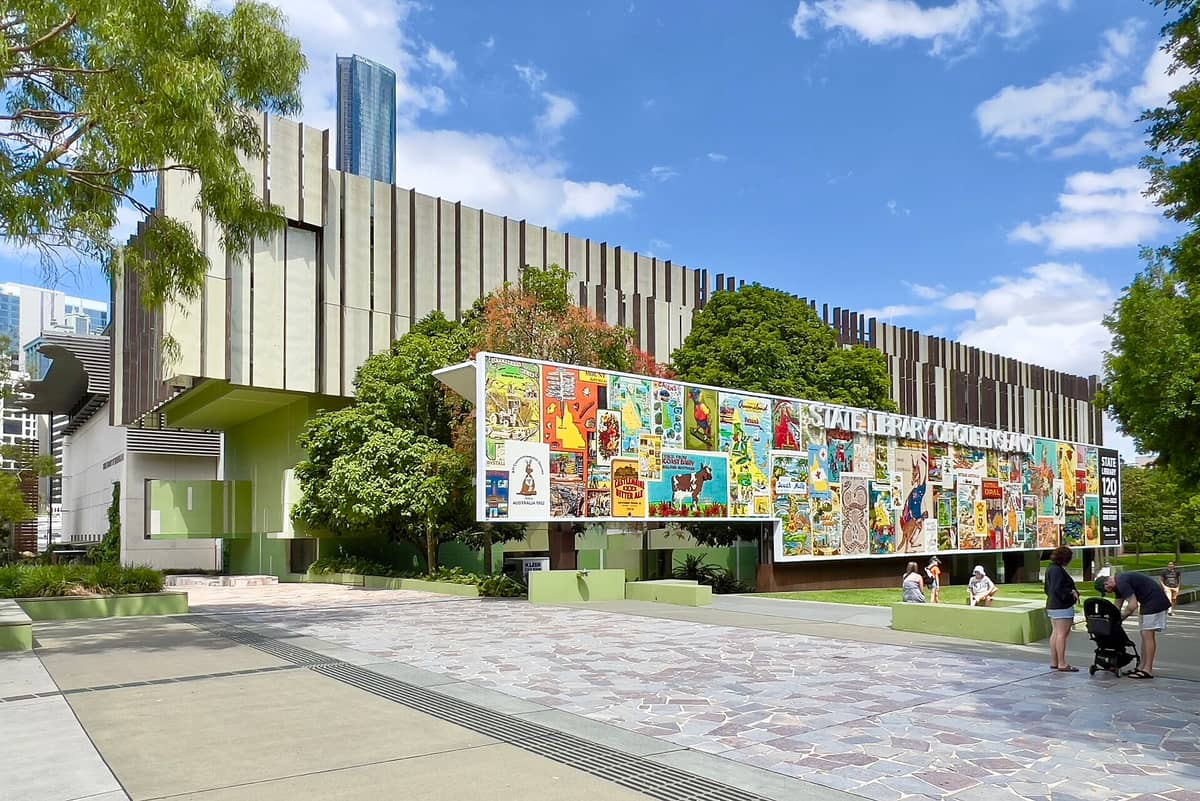Außenansicht der State Library of Queensland in Brisbane mit ihrer markanten modernen Fassade und dem farbenfrohen Wandbild an einem sonnigen Tag.