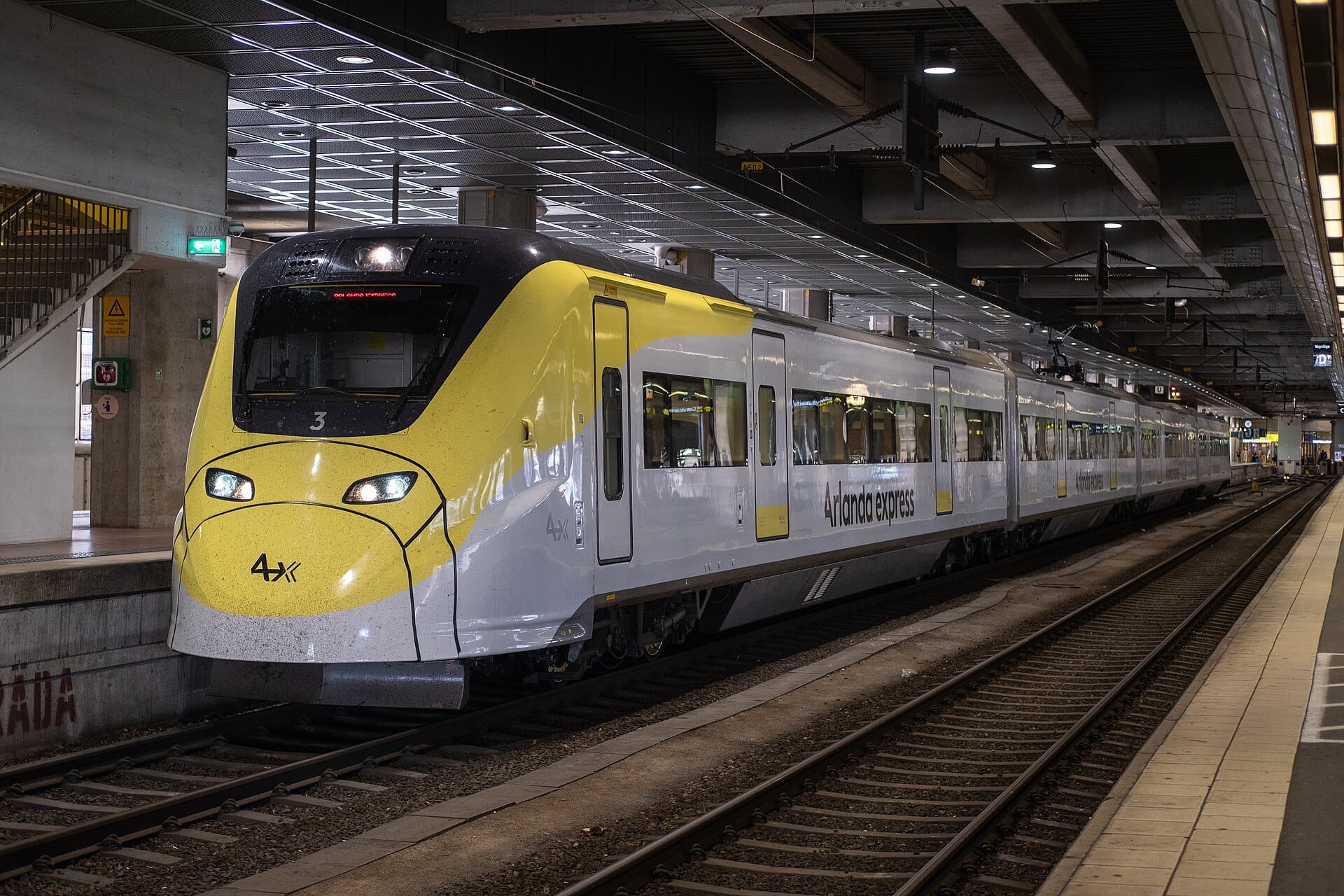 รถไฟความเร็วสูง Arlanda Express บนชานชาลาสถานีในร่มที่ทันสมัย พร้อมชื่อที่มองเห็นได้ชัดเจนที่ด้านข้าง