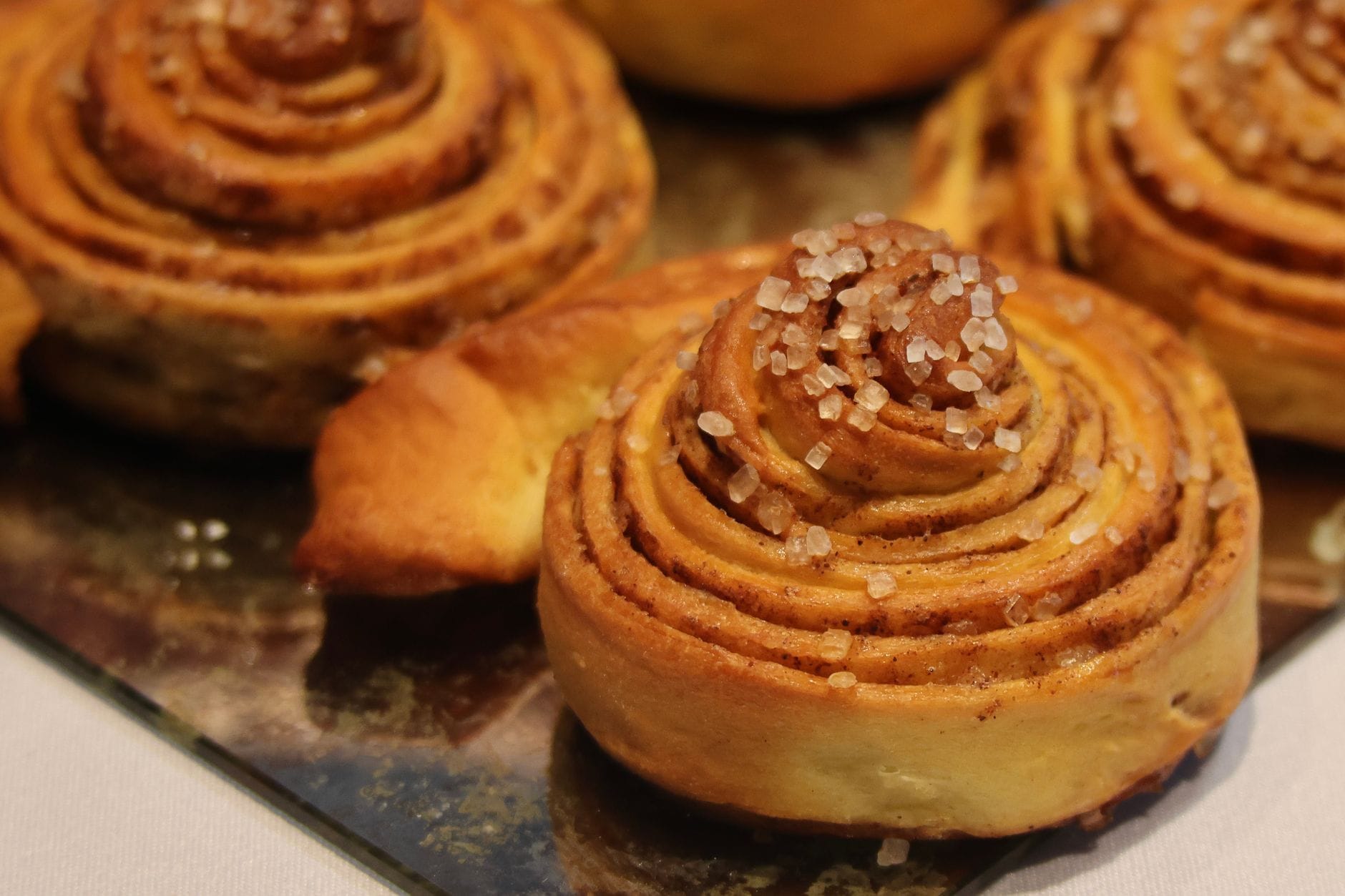 ภาพระยะใกล้ของขนม kanelbullar สไตล์สวีเดนคลาสสิก โรยด้วยน้ำตาลเม็ดมุกบนถาด เผยให้เห็นรูปทรงก้นหอยของขนม