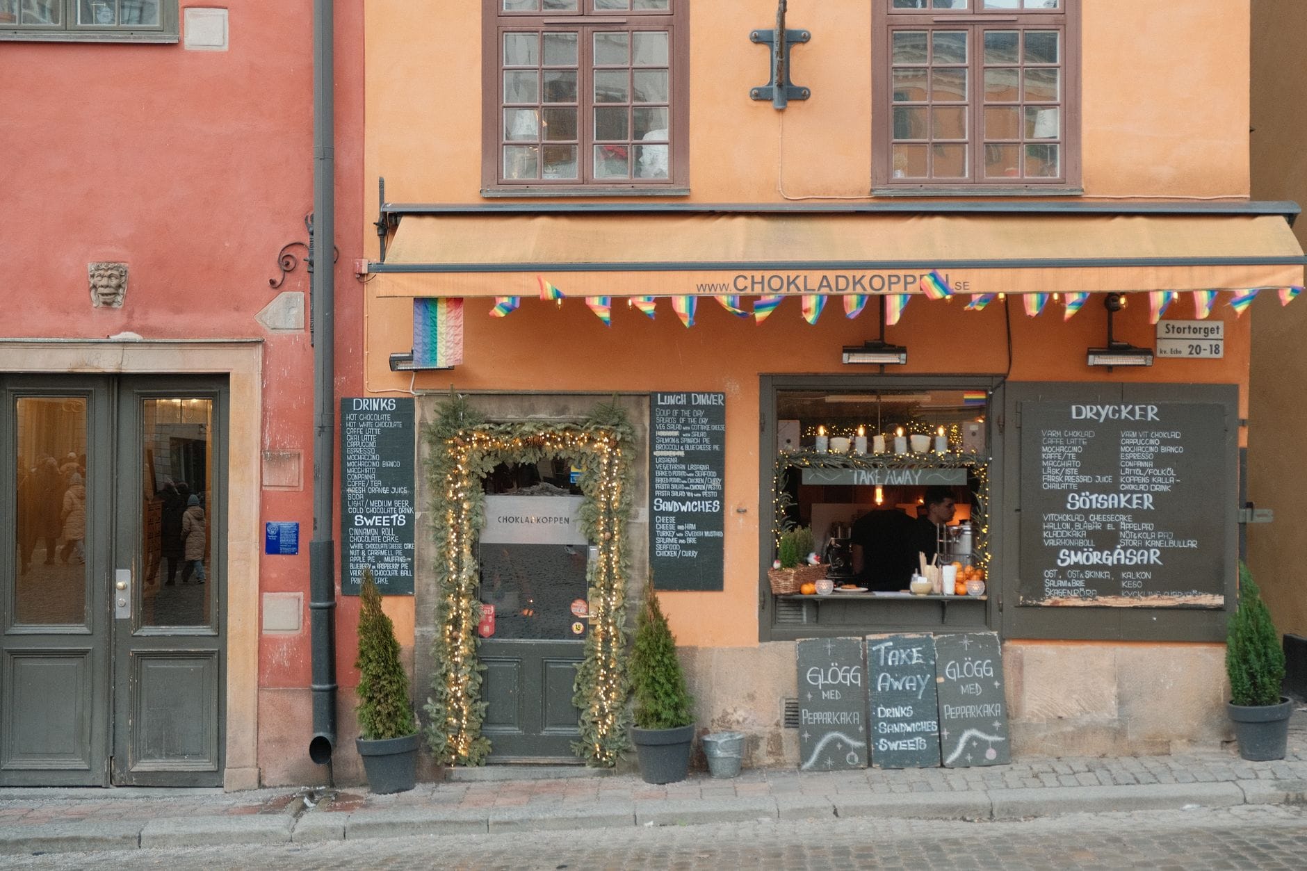 คาเฟ่ Chokladkoppen ใน Gamla Stan กรุงสตอกโฮล์ม พร้อมป้ายเมนูกลางแจ้งและตัวเลือกอาหารซื้อกลับบ้านราคาประหยัดบนถนนหินกรวด