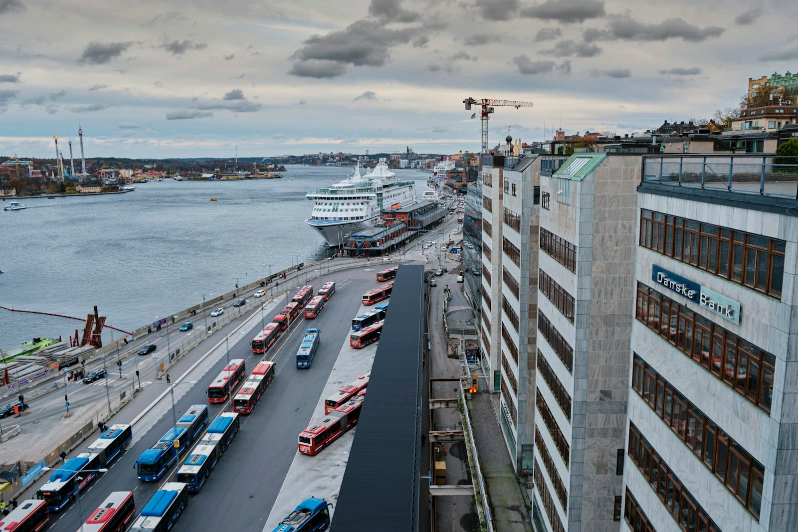 ภาพทางอากาศของท่าเรือเฟอร์รี่ Stockholm พร้อมรถบัสเรียงแถว เรือเฟอร์รี่ขนาดใหญ่จอดเทียบท่า และอาคารริมน้ำโดยรอบ