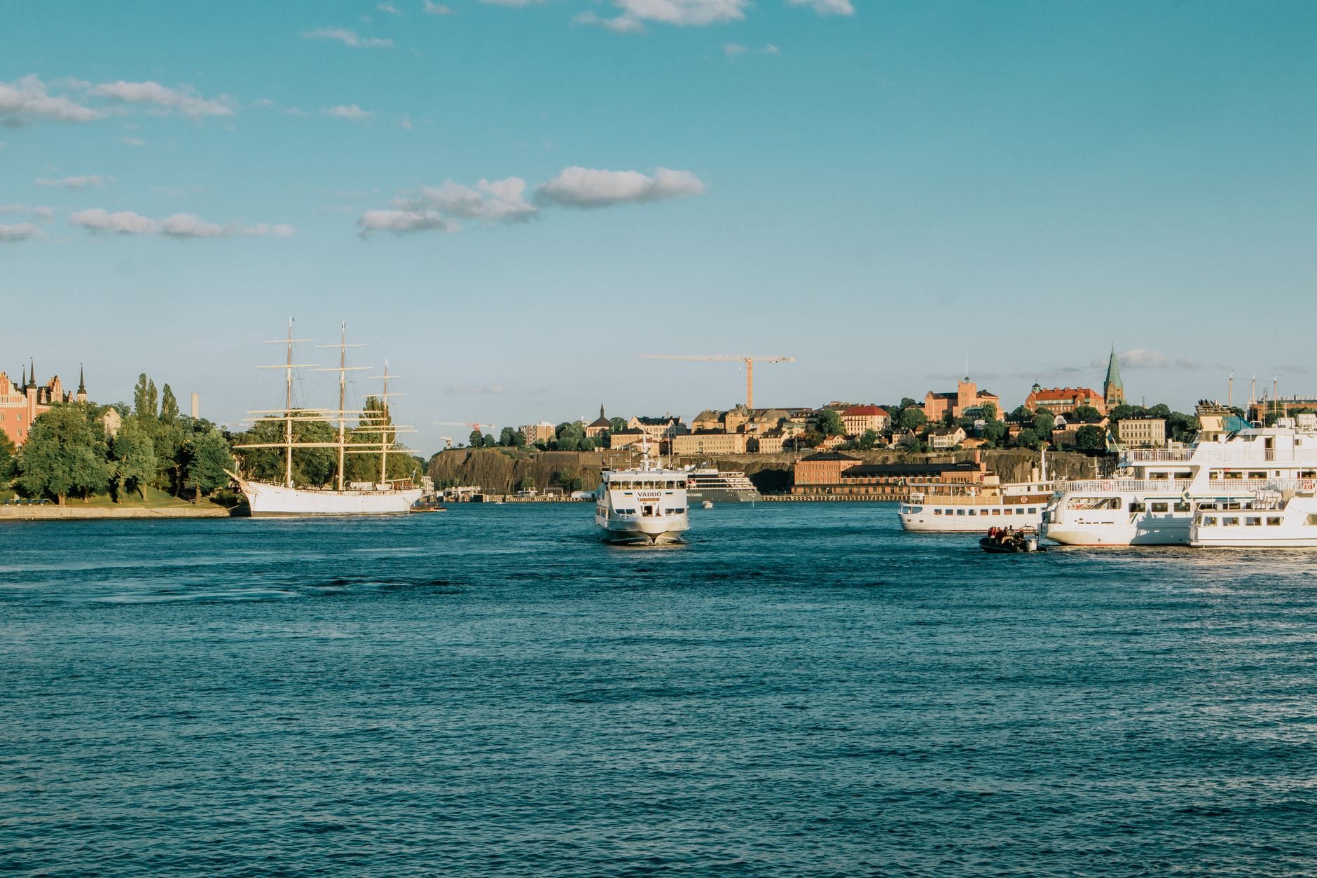 วิวเรือเฟอร์รี่และเรือใบบนน้ำพร้อมเส้นขอบฟ้าเมือง Stockholm และท้องฟ้าฤดูร้อนที่แจ่มใสในพื้นหลัง
