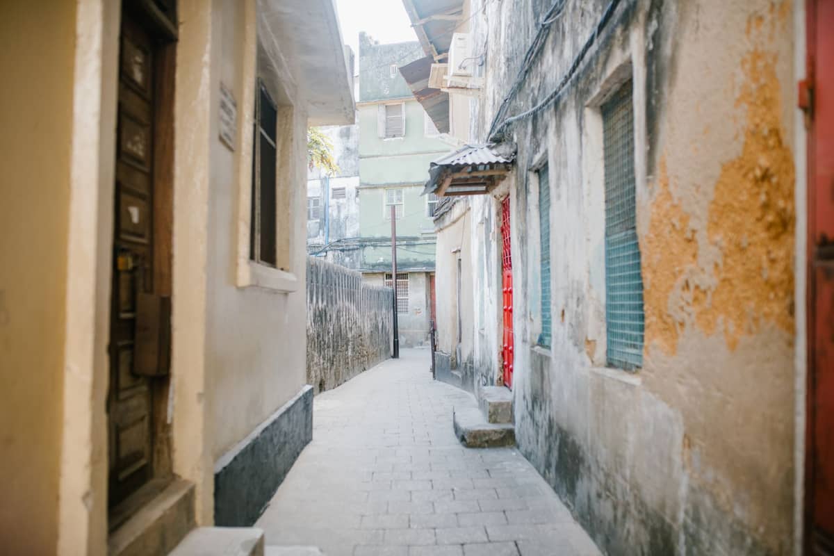 Eine enge, gewundene Gasse zwischen alten Gebäuden mit verwitterten Mauern und kleinen Fenstern, typisch für die historischen Straßen von Stone Town.