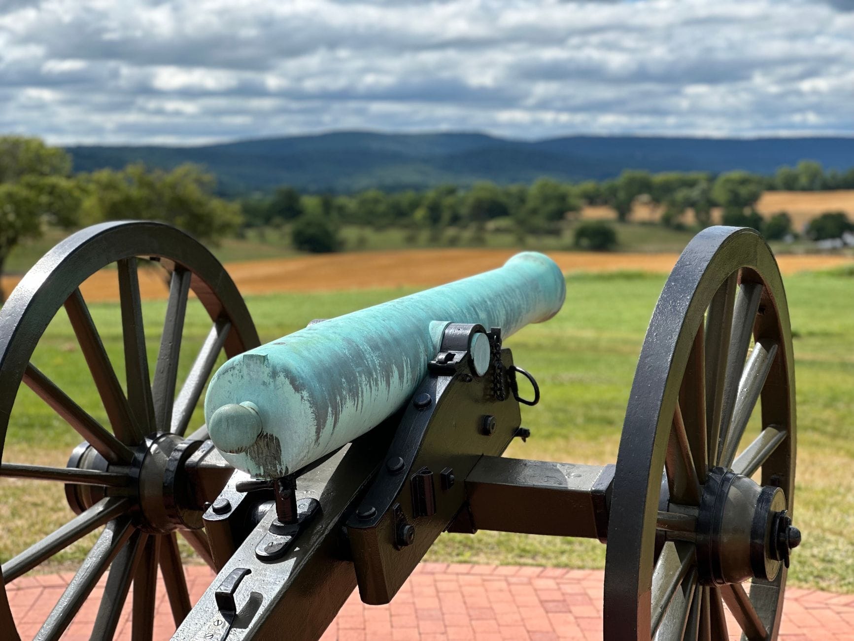 Cañón histórico de la Guerra Civil en Stones River National Battlefield con campos verdes ondulados y colinas distantes bajo un cielo nublado.