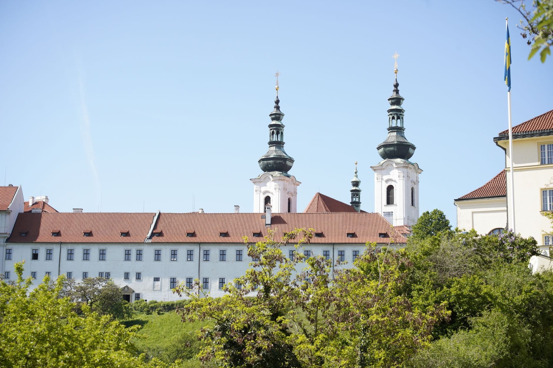 Il Monastero di Strahov a Praga con le sue caratteristiche due torri gemelle, fotografato in una giornata di sole sopra una rigogliosa vegetazione e un cielo azzurro limpido, con la sua architettura barocca in tutto il suo splendore.