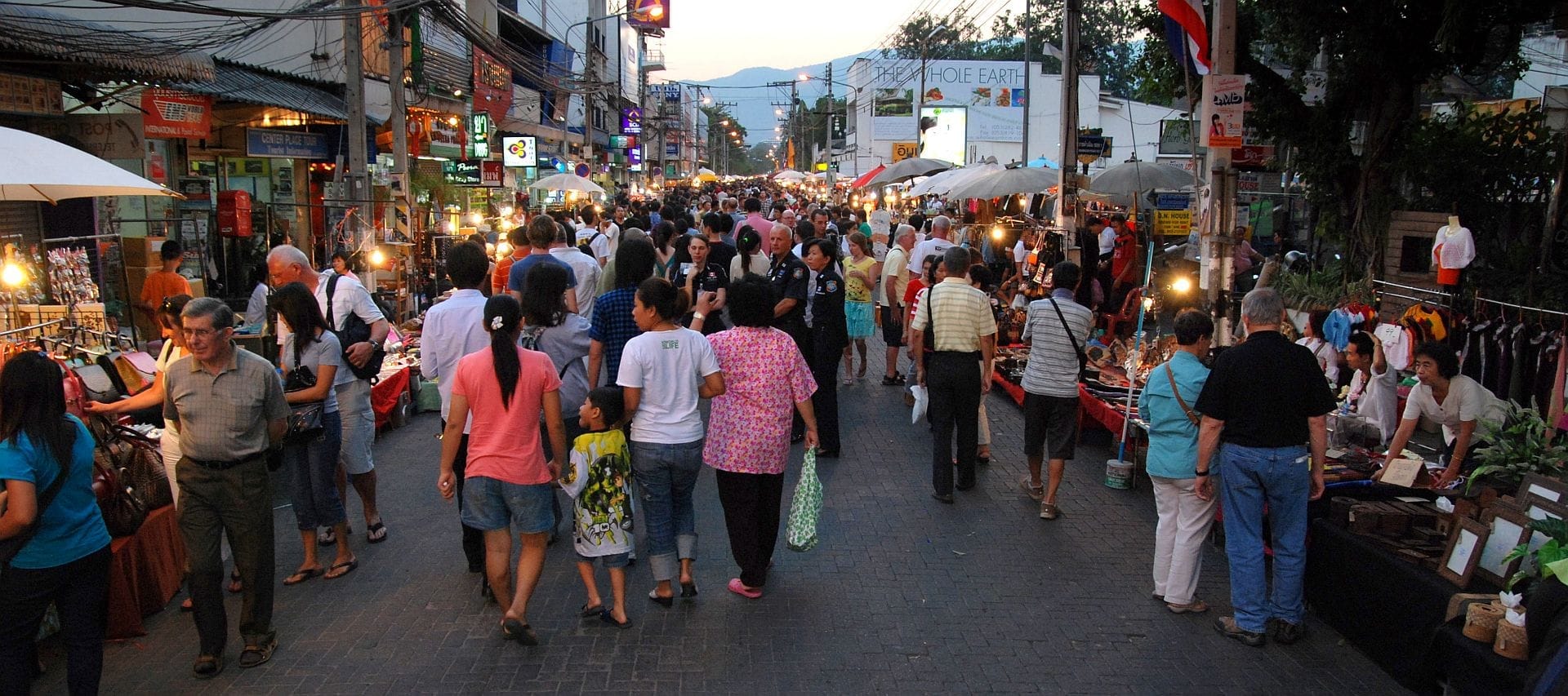 Đám đông đi dạo dọc theo Chiang Mai Sunday Walking Street trên đường Ratchadamnoen, ngắm nhìn các quầy hàng chợ sáng rực và các cửa hàng địa phương lúc hoàng hôn.