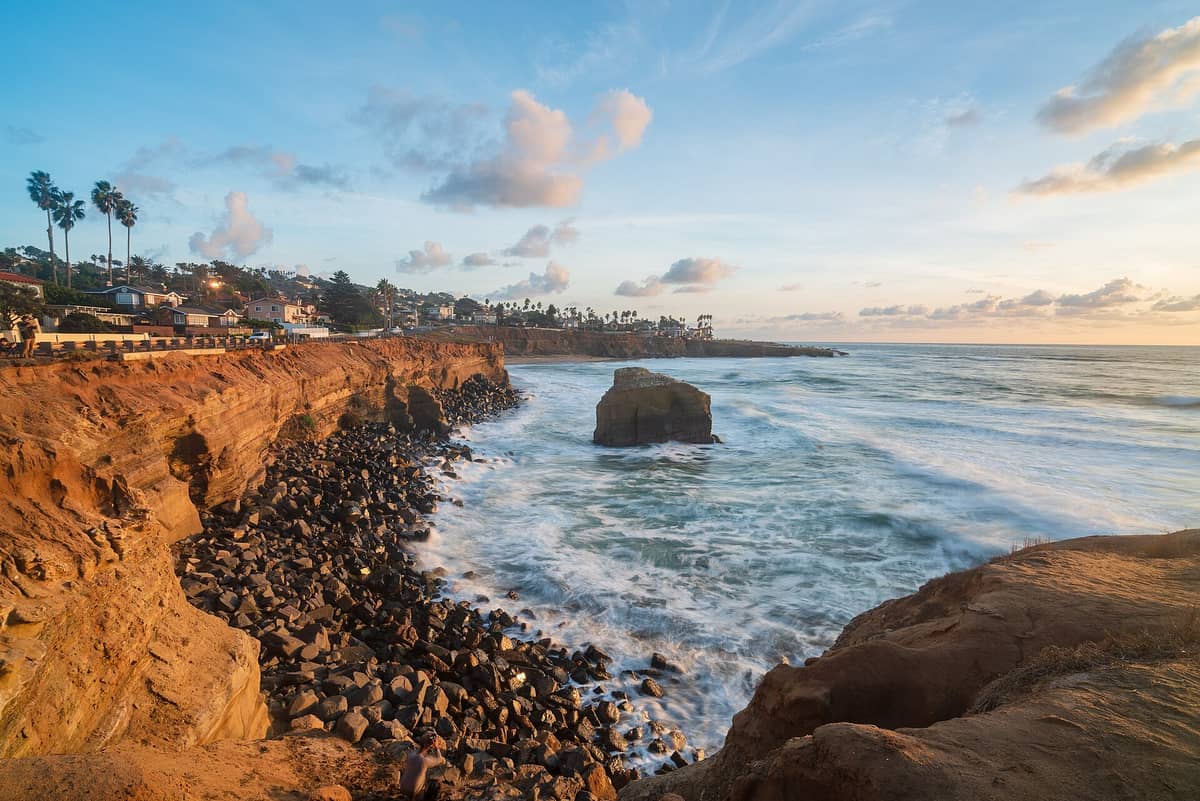 Der Sunset Cliffs Natural Park zeigt zerklüftete Sandsteinklippen, eine felsige Küstenlinie und Meereswellen unter einem teils bewölkten Abendhimmel.