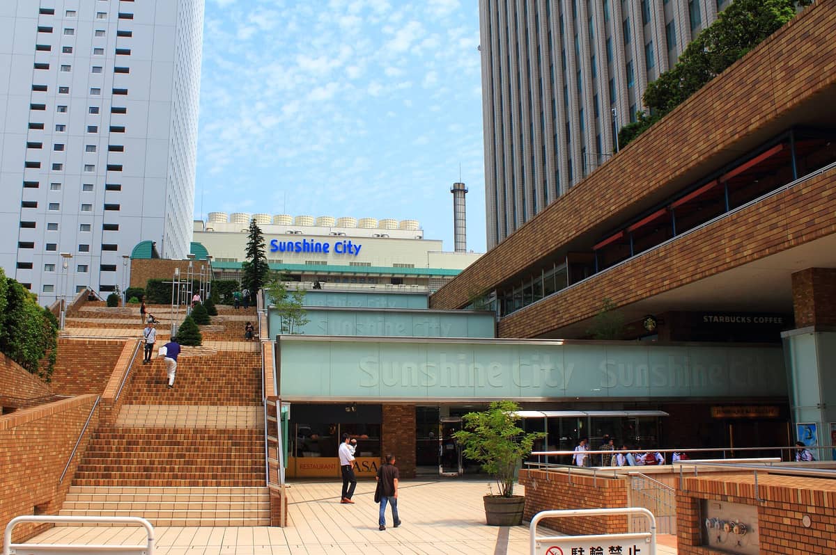 Exterior view of Sunshine City Ikebukuro with its distinct brick plaza, steps, high-rise buildings, and a visible Sunshine City sign in Tokyo.