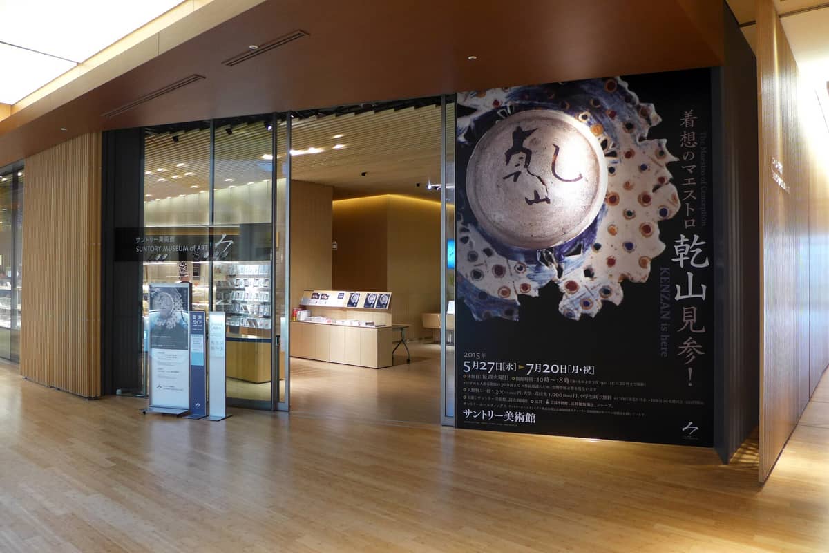 Entrance to the Suntory Museum of Art inside Tokyo Midtown, showing large exhibition poster, museum signage, glass doors, and modern wood interior.