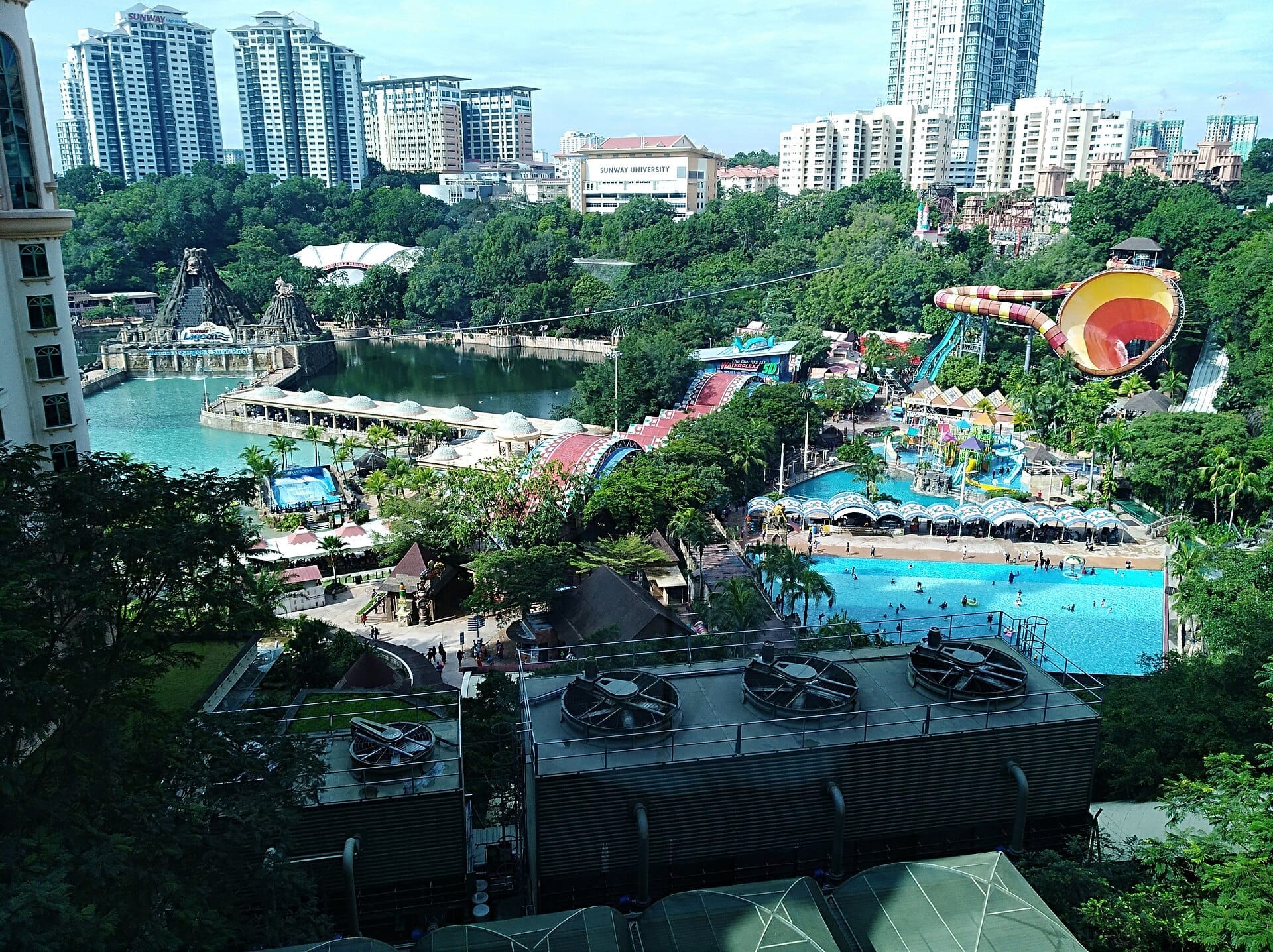 View over Sunway Lagoon theme park with pools, colorful water slides, lush greenery, and surrounding high-rise buildings in Kuala Lumpur.