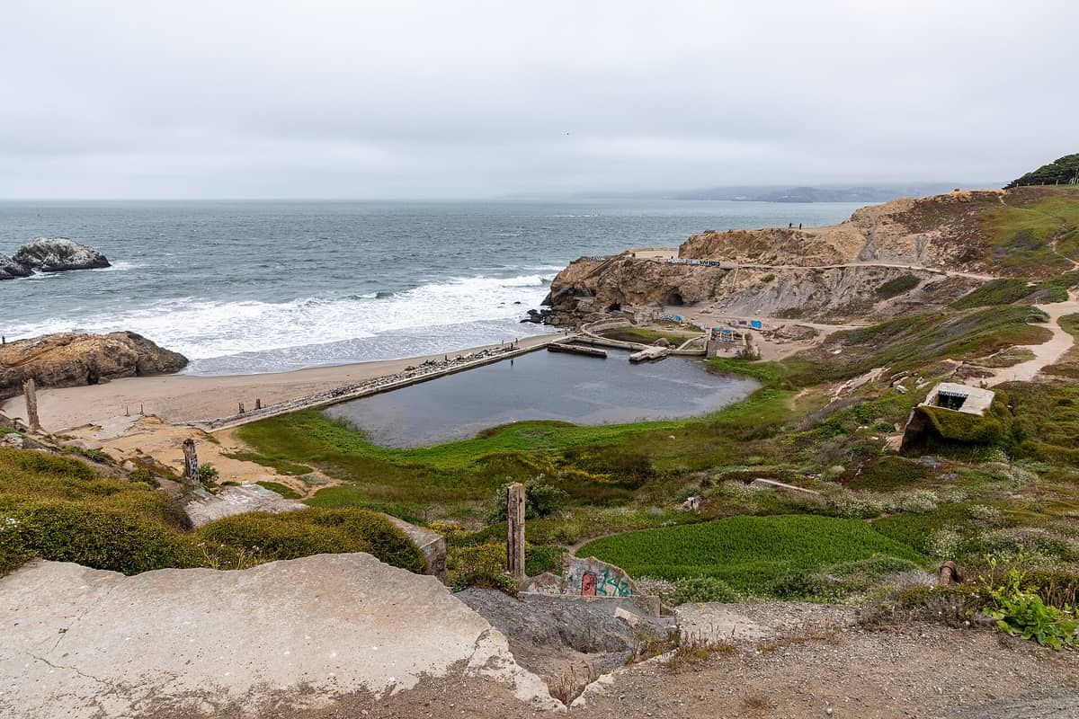 Weitläufige Ansicht der Betonruinen und Becken der Sutro Baths an der Küste San Franciscos, mit brechenden Wellen im Hintergrund und felsigen Klippen in der Nähe.