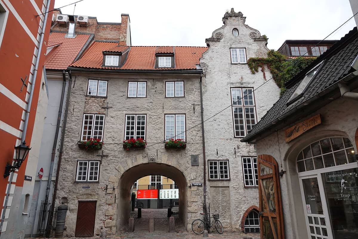 Klare Gesamtansicht des Schwedischen Tors in Riga – ein historisches Stadttor mit Bogendurchgang durch ein Steingebäude, rotem Ziegeldach und Kopfsteinpflasterstraße.