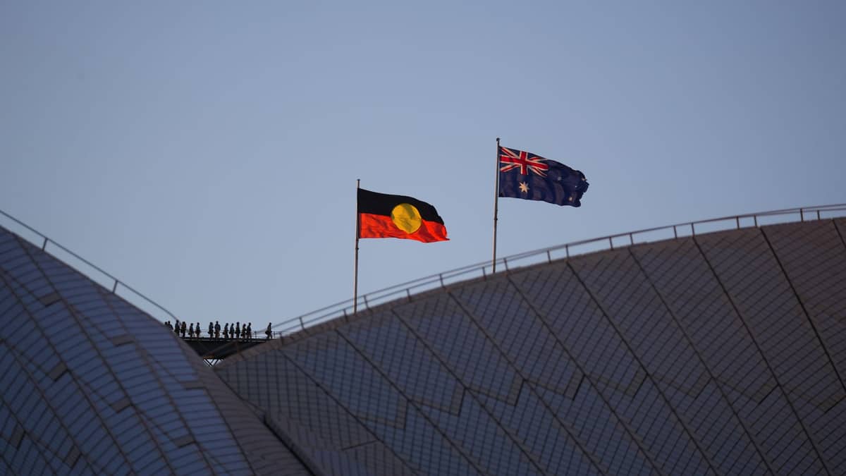 Flagi Aborygenów i Australii powiewają na szczycie Opery w Sydney na tle błękitnego nieba, symbolizując kulturę i historię rdzennych mieszkańców.