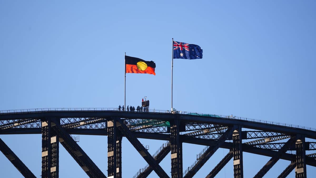 Close-up of Sydney Harbour Bridge with the Aboriginal and Australian flags flying at the top against a clear blue sky.