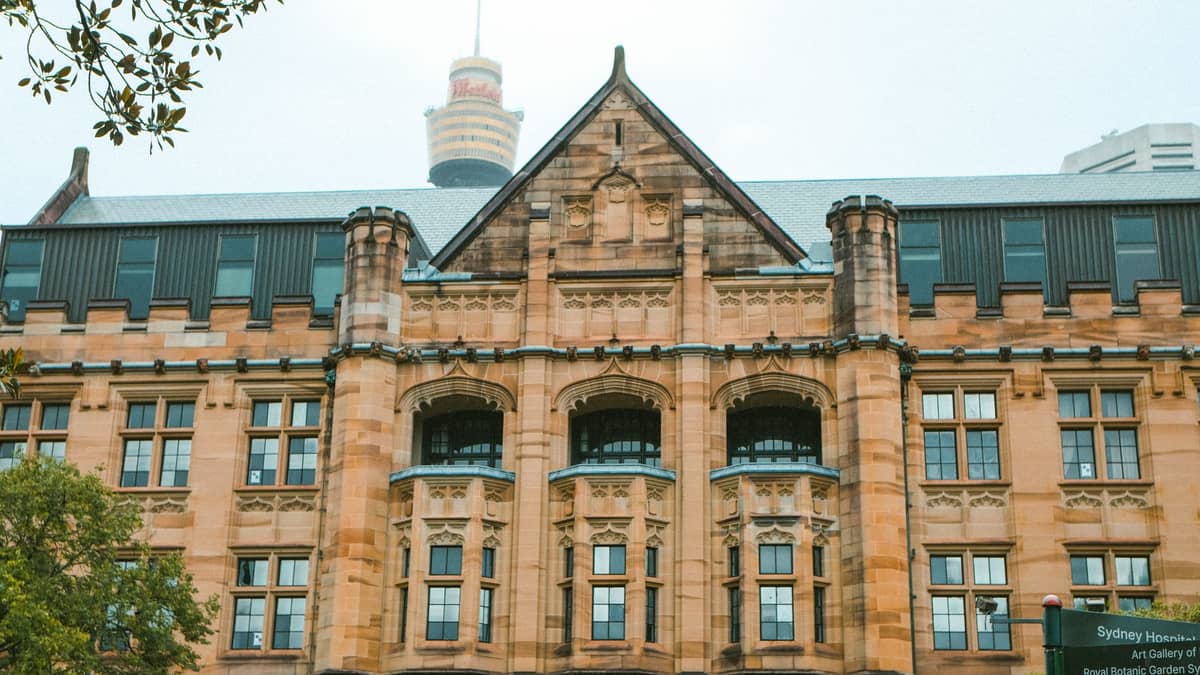 Historic sandstone facade of the Australian Museum in Sydney, with Sydney Tower visible in the background on a foggy day.