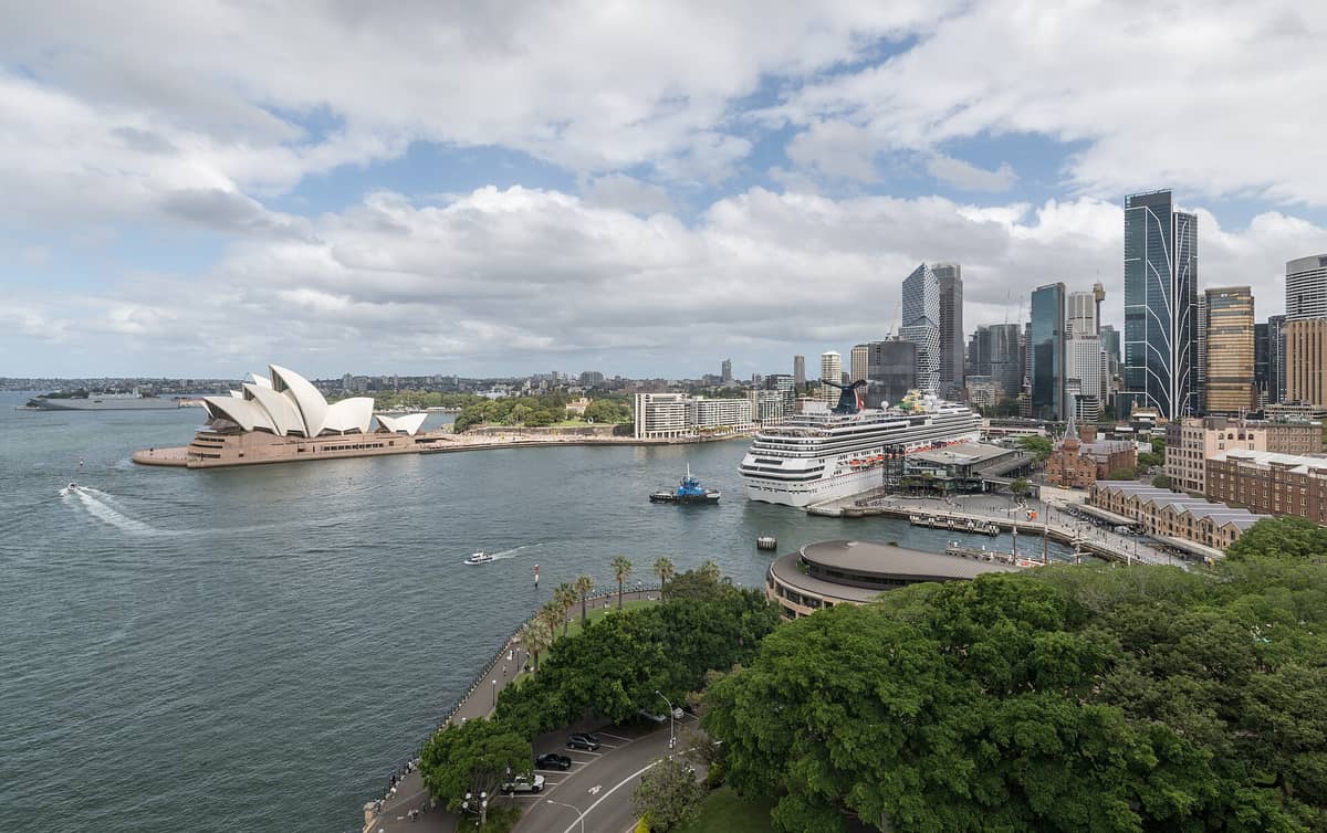 มุมกว้างใจกลางเมืองซิดนีย์เห็น Circular Quay, โรงอุปรากร ซิดนีย์, ตึกสูง และท่าเรือติดอ่าวในวันที่มีเมฆบางส่วน