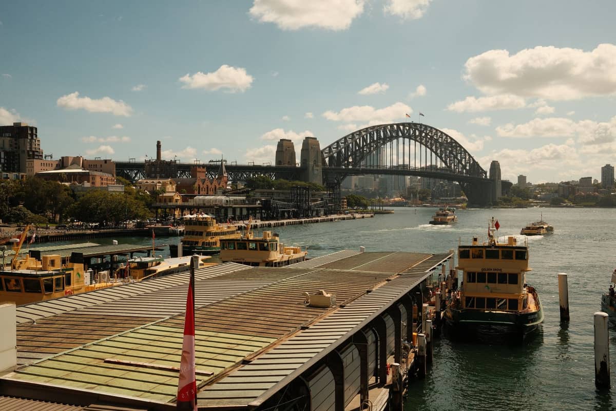 Fähranleger am Circular Quay mit mehreren angedockten Sydney Ferries, Sydney Harbour Bridge im Hintergrund unter einem teilweise bewölkten Himmel.