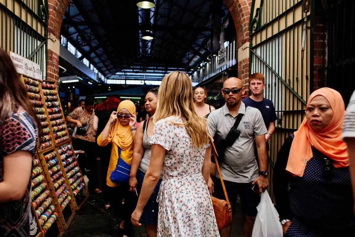 Maingay na pasukan ng loob na palengke na may iba't ibang mamimili at tindahan, katulad ng Paddy's Markets Haymarket sa Sydney.