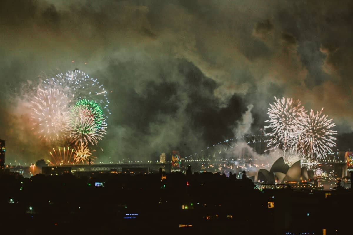 Sydney Harbour nocą podczas sylwestrowych fajerwerków — przez kolorowy dym wyraźnie widać Operę Sydney i Most Harbour Bridge.