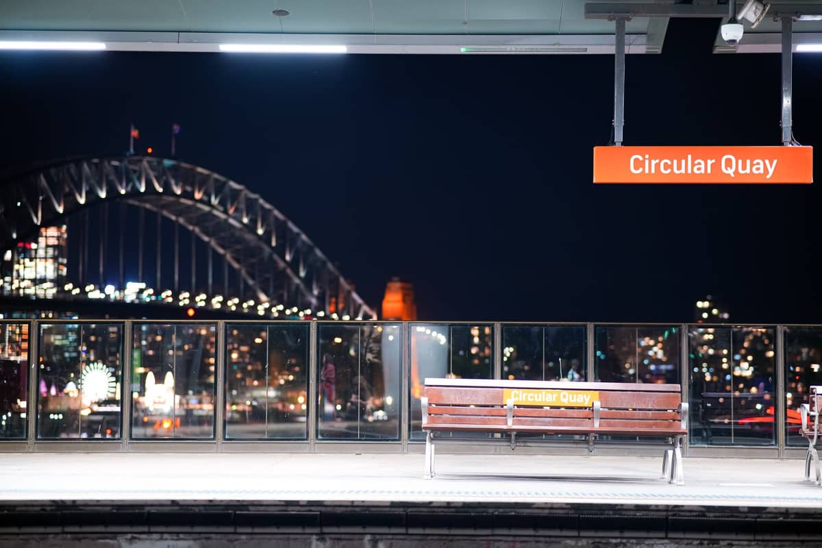 Andén de la estación de tren de Circular Quay en Sídney de noche con vistas al Harbour Bridge y el horizonte de la ciudad al fondo.