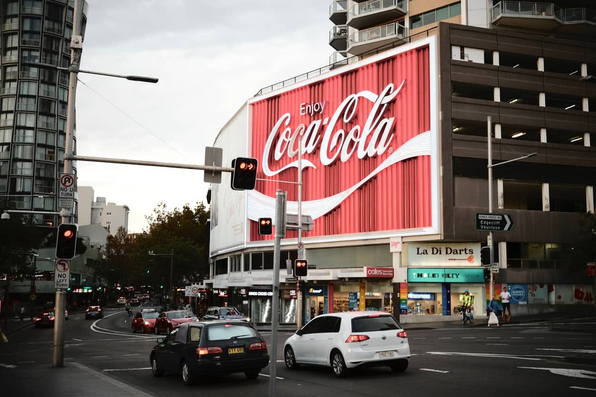 View of Kings Cross at dusk with the iconic Coca-Cola sign lit up and cars driving by, an emblem of Sydney nightlife history.