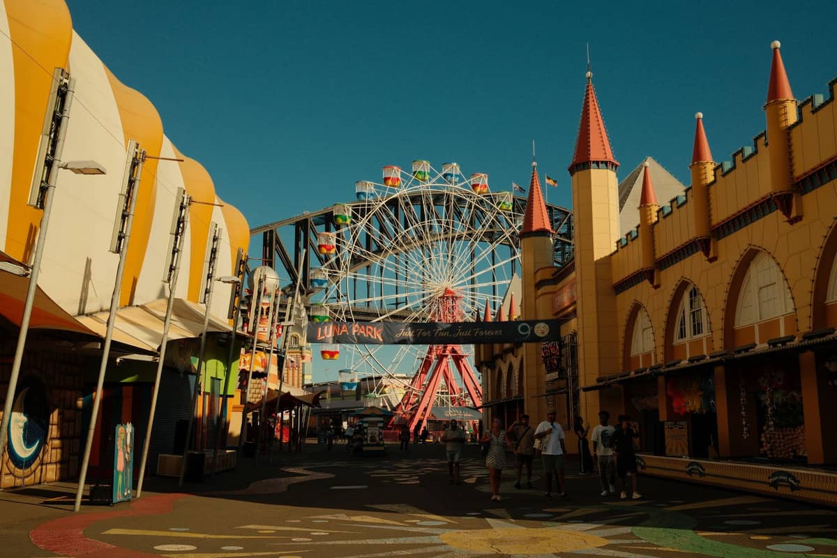 Wejście do Luna Park Sydney z kolorowymi budynkami, kołem Ferris i Mostem Harbour Bridge w tle w słoneczny dzień.