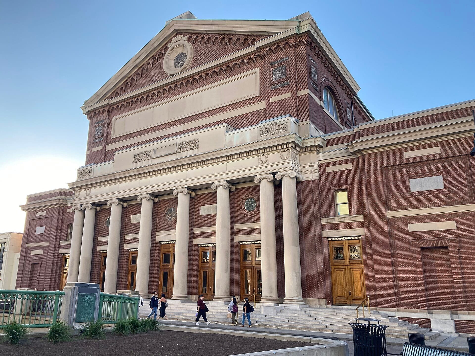 La facciata neoclassica della Symphony Hall di Boston, con alte colonne, muri in mattoni rossi e visitatori che salgono i gradini sotto un cielo sereno.