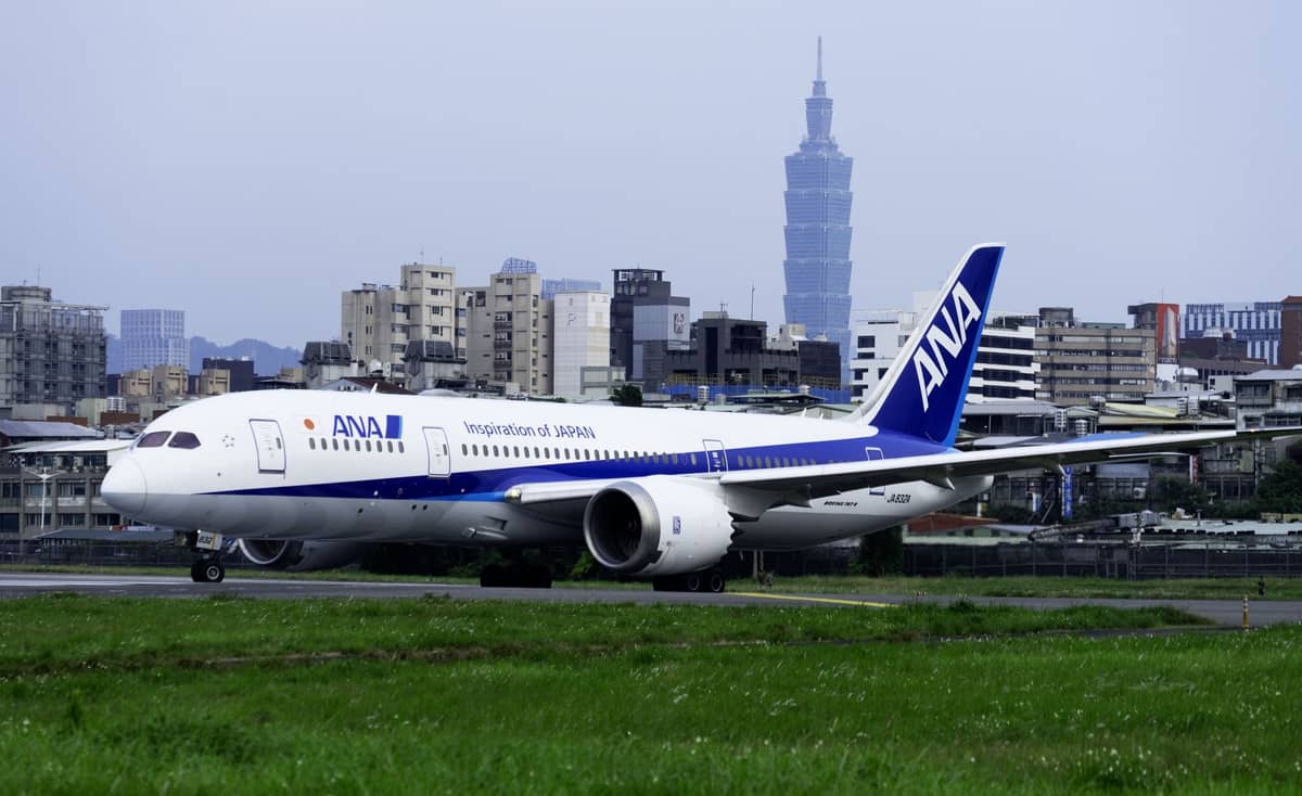 Ein ANA-Flugzeug auf der Startbahn des Taipei Songshan Airport mit dem Taipei 101 und der Stadtsilhouette im Hintergrund.