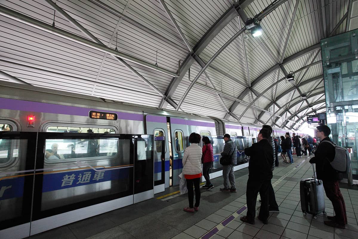 Reisende mit Gepäck warten auf den Taoyuan Airport MRT-Zug auf einem modernen Bahnsteig in Taipei.