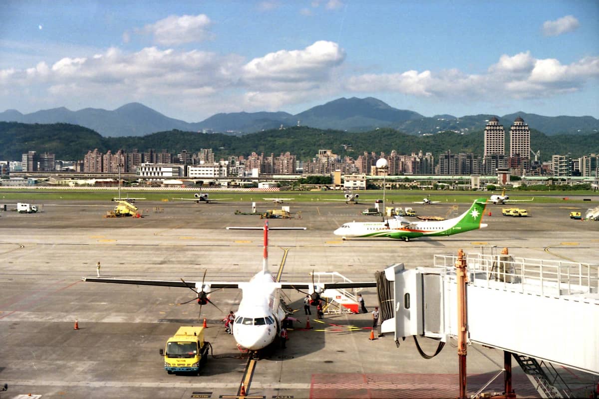 Blick auf das Vorfeld des Flughafens Songshan mit Flugzeugen, der Skyline von Taipei und den umliegenden Bergen im Hintergrund unter blauem Himmel