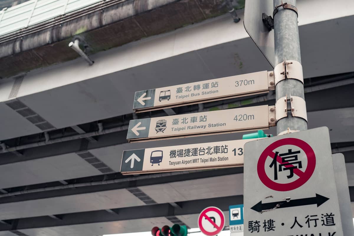 Straßenschild in Taipei mit Wegweisern zur Taipei Bus Station, zur Taipei Railway Station und zur Taoyuan Airport MRT, unter einer Überführung.