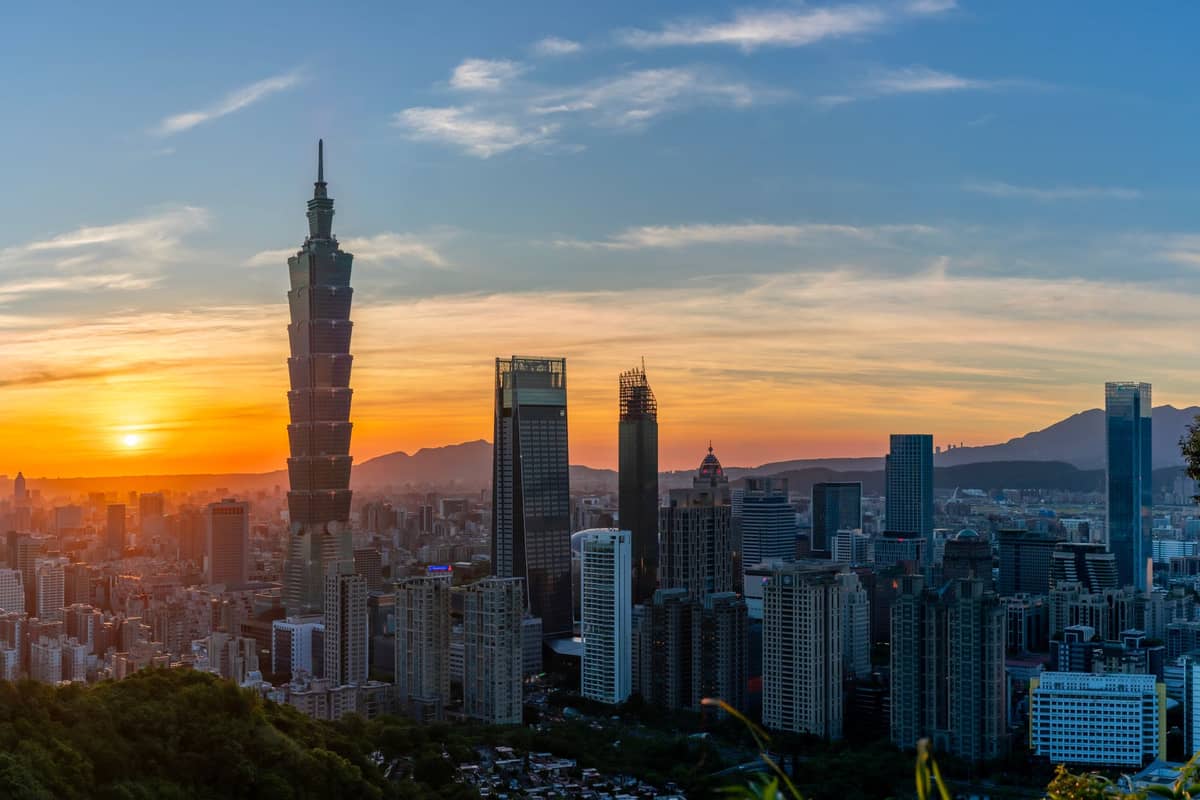 Skyline von Taipei bei Sonnenuntergang mit Taipei 101 und modernen Hochhäusern vor einer Bergkulisse.